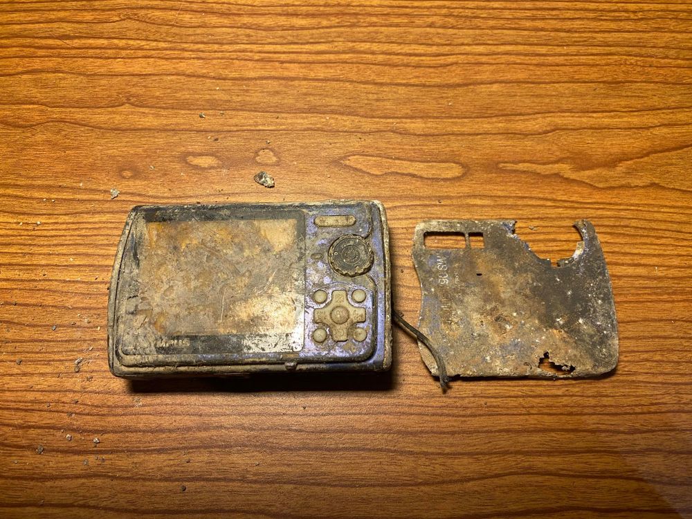 Mud-covered, broken digital camera on a wooden surface