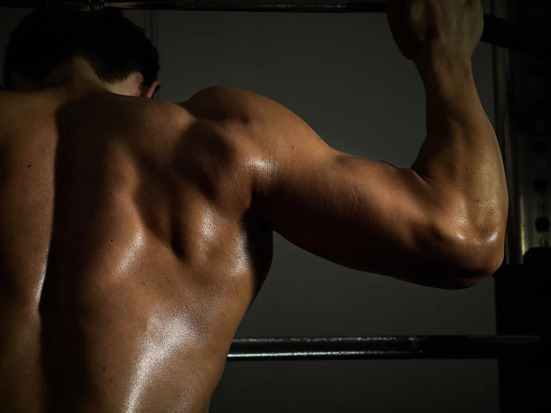 half the back and one arm of a man flexing muscle in dim light