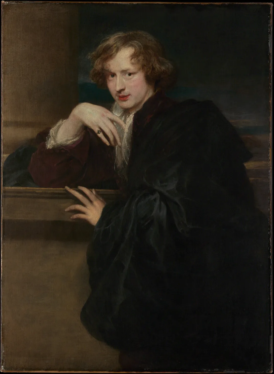 A self portrait of a young man with blonde wavy hair, posing in dark clothes with his hands positioned in front and under his chin
