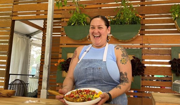 Candid photo of Elena Terry smiling holding a white dish full of colorful beans, peppers, and corn tilted away from her.