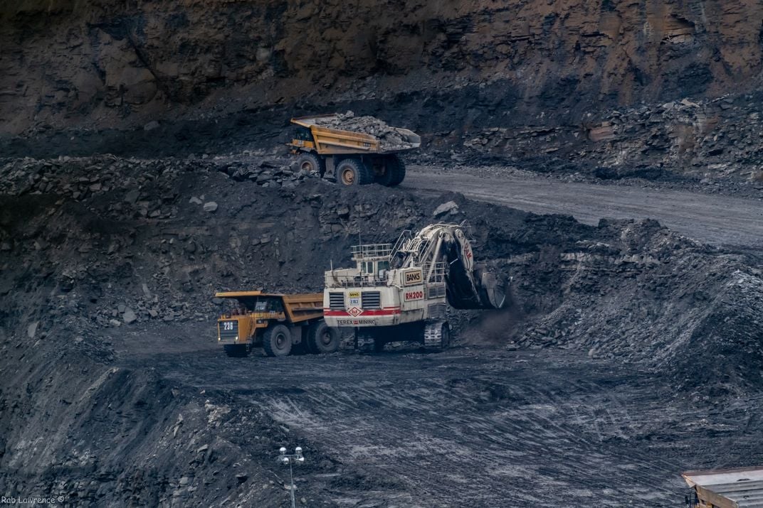 Three trucks drive and load coal in a mine in England