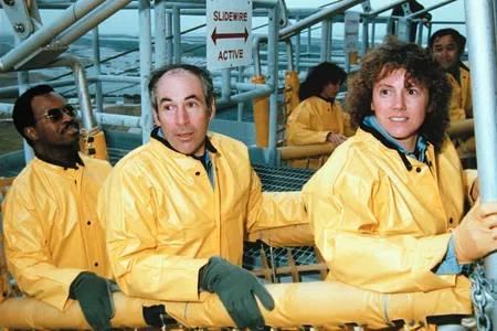 Members of the STS-51L Challenger crew practice emergency escape from the launch pad in preparation for their January 1986 launch. From left: Ron McNair, Greg Jarvis and Christa McAuliffe. In the background are Judy Resnik and Ellison Onizuka.