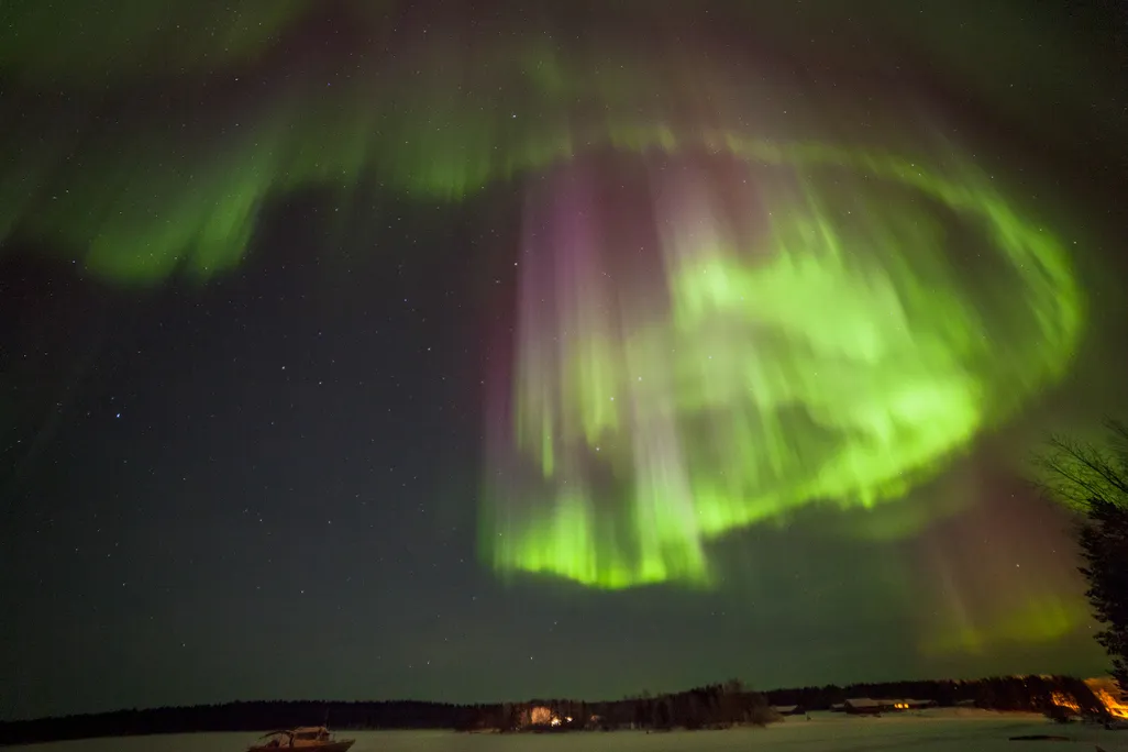 An image of the northern lights over Lake Inari in Finland. The lights are a glowing green and purple.