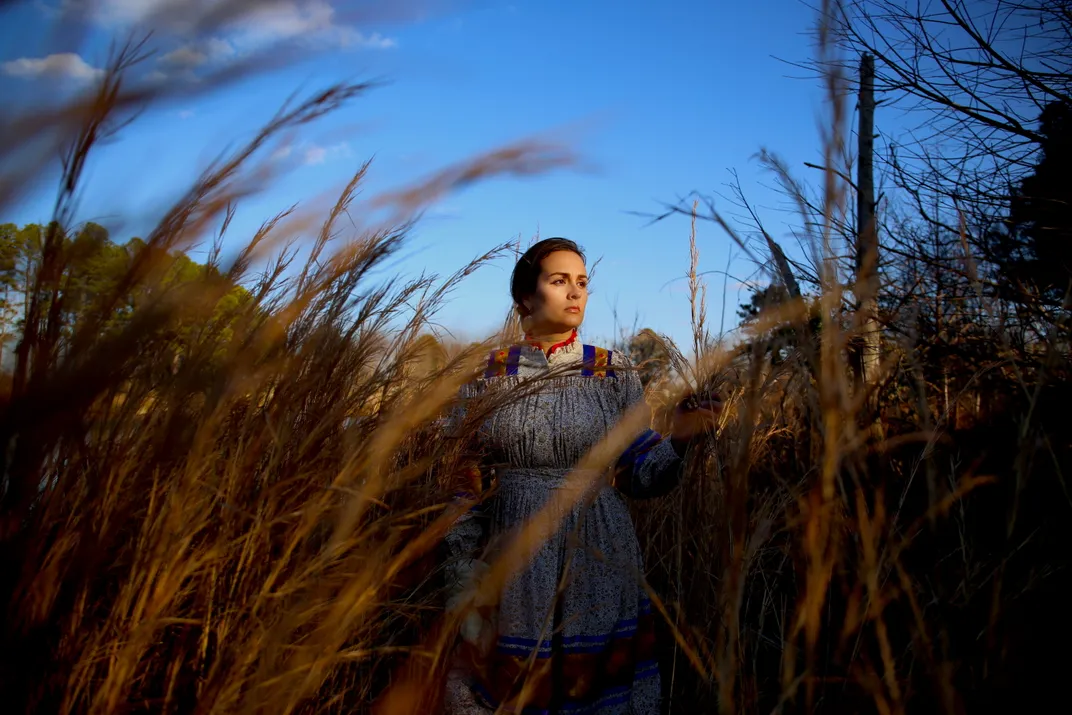 A Cherokee women in traditional garb stands in a field of tall grass