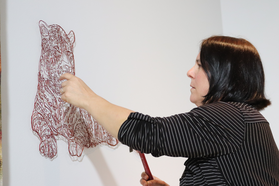 Artist nails string in the shape of a jaguar to a white wall