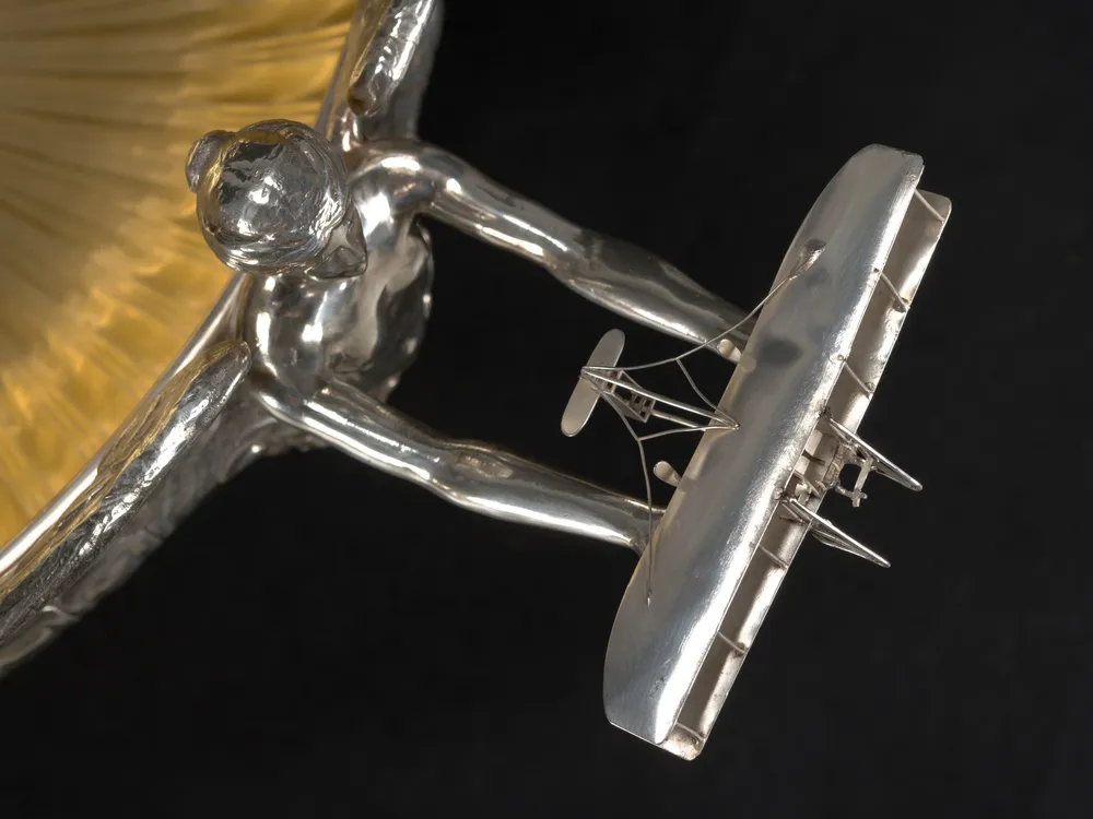 Overhead detail view of a trophy showing a silver angel extending her arms holding a vintage airplane.