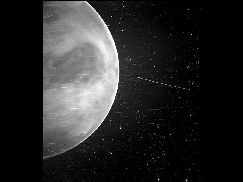 A letterboxed image with NASA's new Venus placed vertically at the center. Half of the planet is positioned on the left part of the picture with celestial objects zooming by and stars in the background
