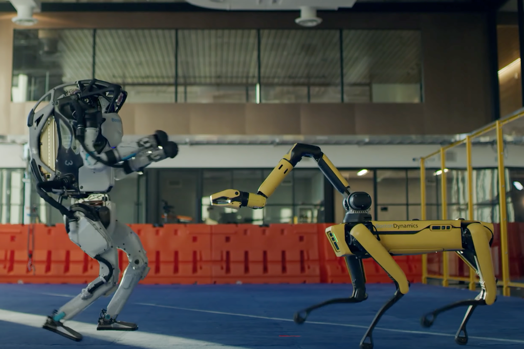 The humanoid Atlas robot dances on the left side of the image, and the canine-like Spot robot dances on the right