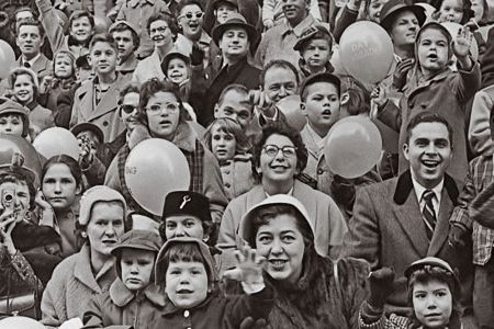 A crowd of people cheering and waving at a parade, circa 1955.