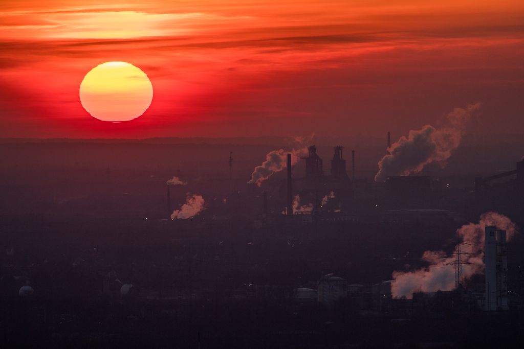 A setting sun over emissions billowing from buildings on the ground.