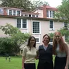 Three women pose for a photo in front of a Victorian-style house.