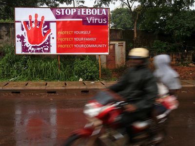 People ride past a board with control and prevention information of the Ebola epidemic outbreak in the Ebola-affected Freetown, capital of Sierra Leone, Aug. 17, 2014.