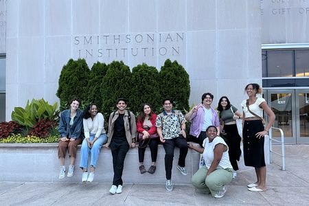 A group of student interns gather in front of a grey building