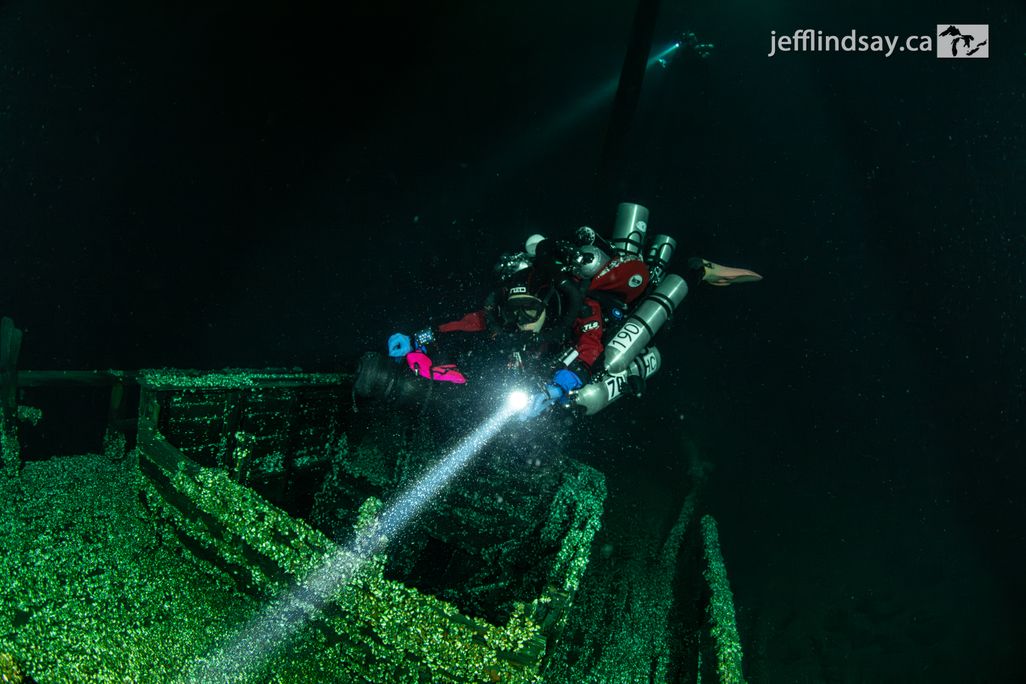 A diver with a flashlight swimming over a shipwreck