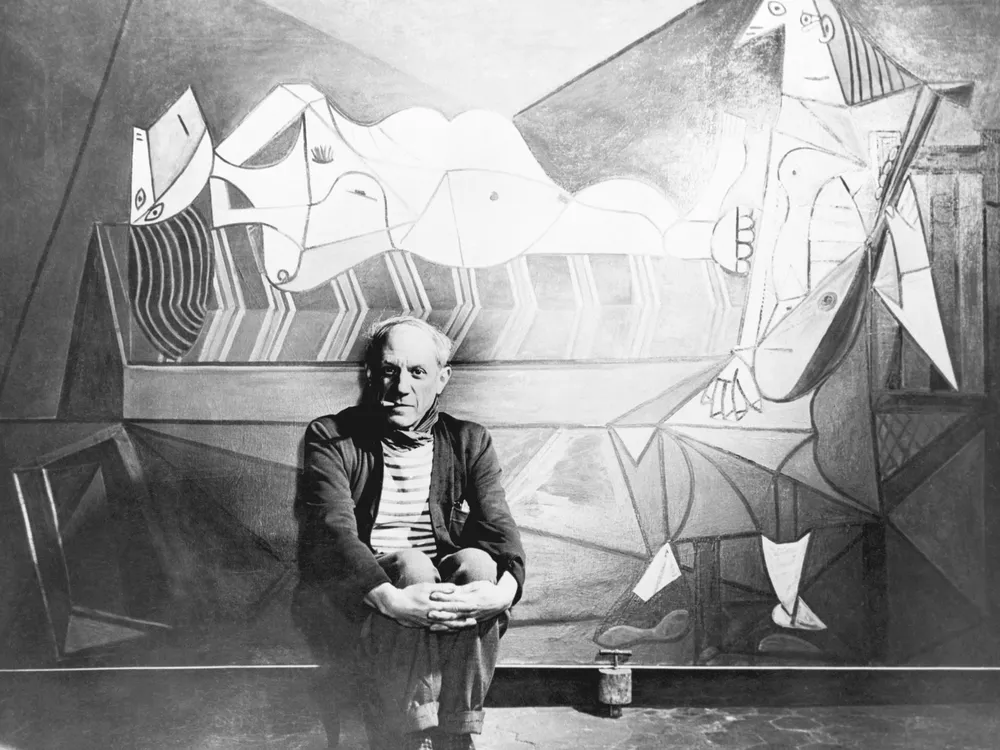 Black and white image of Pablo Picasso posing in front of one of his paintings