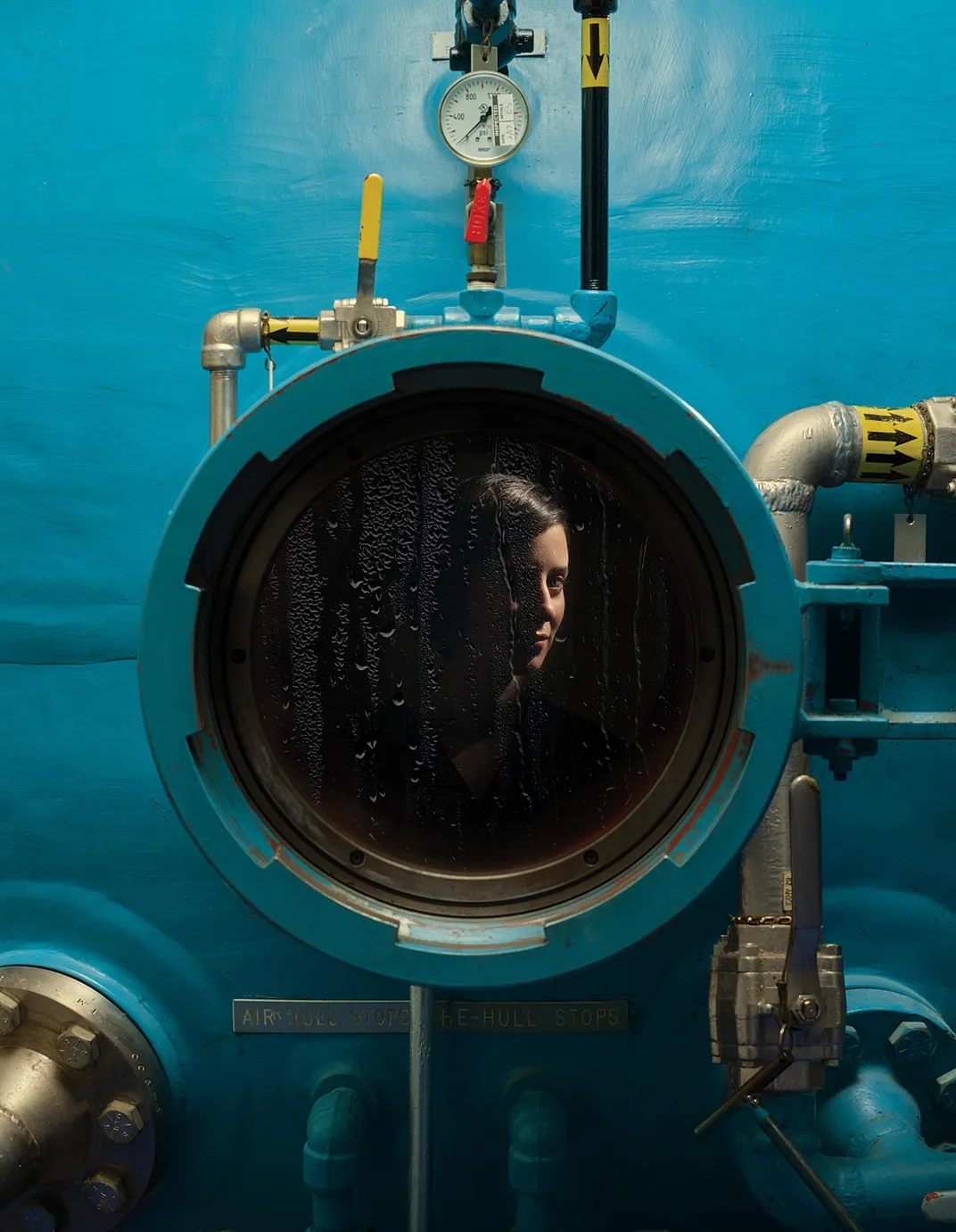 Rachel Lance looking out of a porthole of a hyperbaric chamber