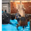 A group of students in bright blue shirts gather around a statue of George Washington with a museum facilitator
