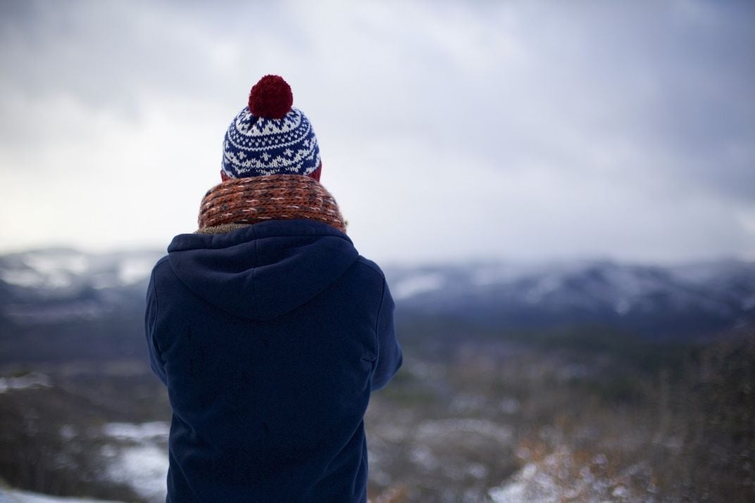 A person wearing a knit hat and scarf standing on a cliff.