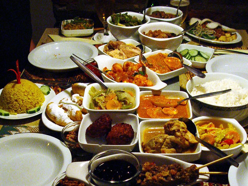 A dining table set with more than a dozen dishes of food, including white rice, meat on skewers, stewed vegetables, and sliced cucumbers.