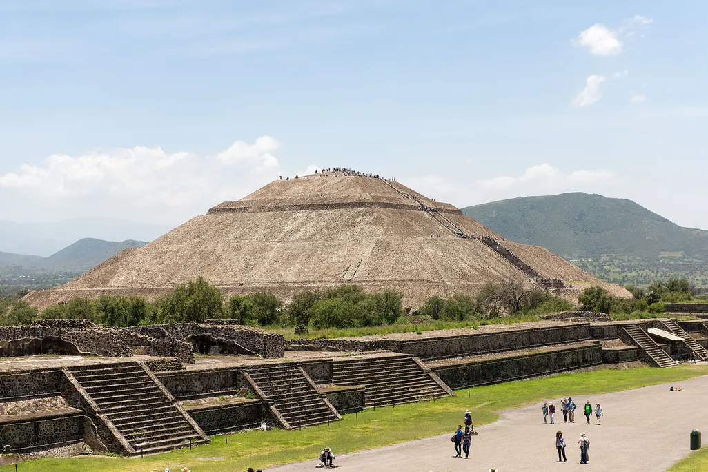 A view of the Pyramid of the Sun at Teotihuacan, a huge pyramid that stands several stories tall over an expansive avenue populated by tourists