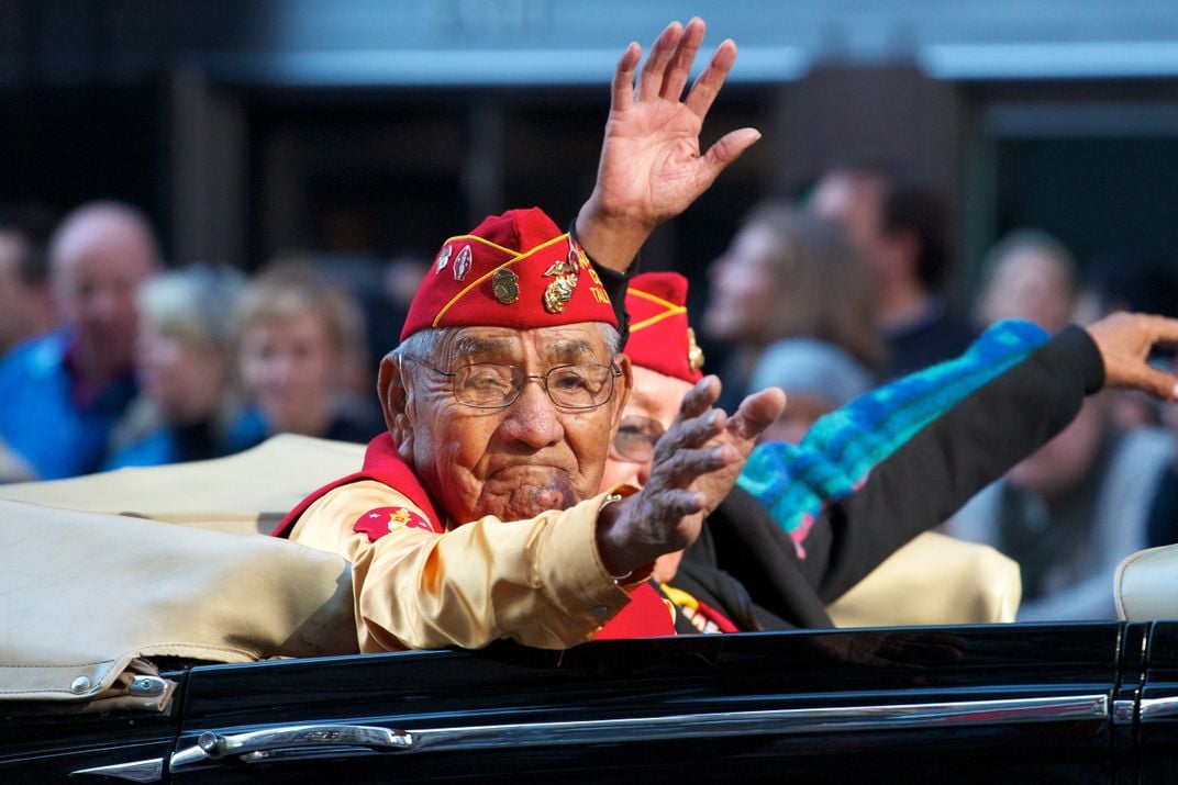 a Navajo Code Talker waves from a car in a parade