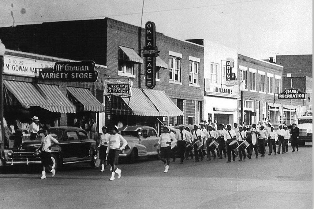 View of an unspecified parade on Greenwood Avenue, Tulsa, Oklahoma, 1930s or 1940s. Among the visible businesses are the offices of the Oklahoma Eagle newspaper at 117 North Greenwood Avenue