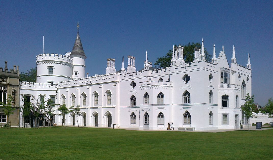 A large white castle-like mansion, with round turrets and spires, all a bright white against a blue sky and green grass