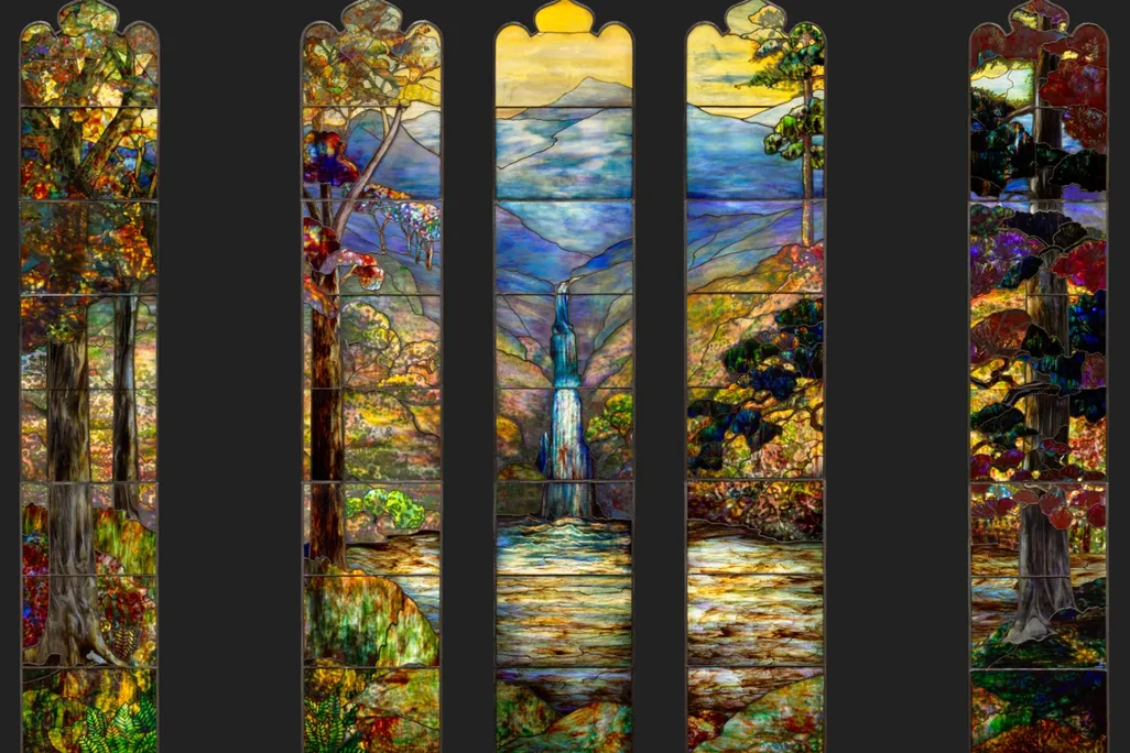 Five thin panels of stained glass, two on either side and three grouped closely together, depict a colorful landscape with blue mountain in the background and a waterfall flowing into a yellow green pond