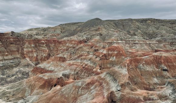 A grey, orange, and brown expanse of layered rock formations under a gray sky.