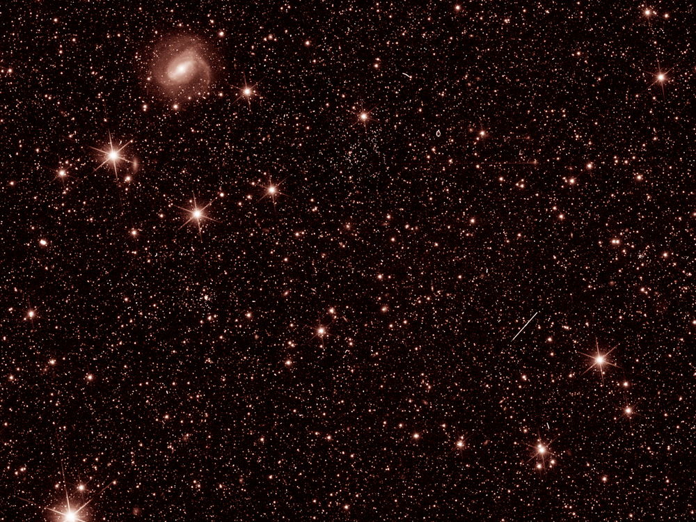 An image of outer space showing distant stars and galaxies in a light red color