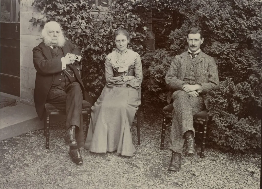 From left to right, a man in a dark suit seated in a chair with white muttonchops, a brown haired young woman in plain lightcolored dress, and a man with brown hair and a mustache in tan suit in sepia colored image