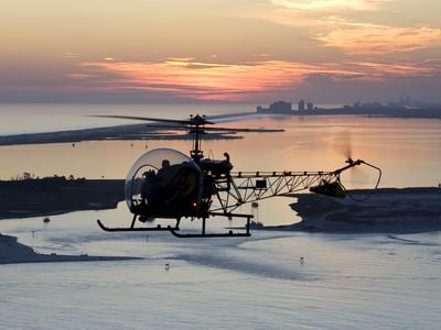 The trademark plexiglass sphere enclosing its cockpit gave the Bell 47 its nickname and provides the pilot cruising this beach a glorious view of a Florida sunset.