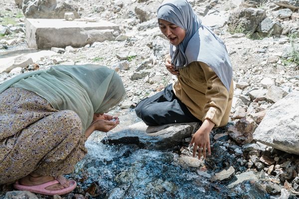 Two Muslim girls drink water from a stream. thumbnail