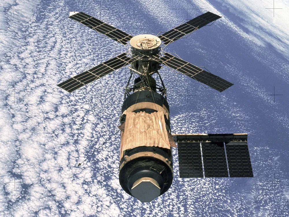 skylab from space, a cylinder with four solar panels forming a propeller shape on its upper area and one solar array wing extending to the right side