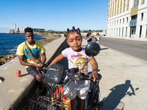 A young girl sits on her father's motorcycle by the water in Havana thumbnail