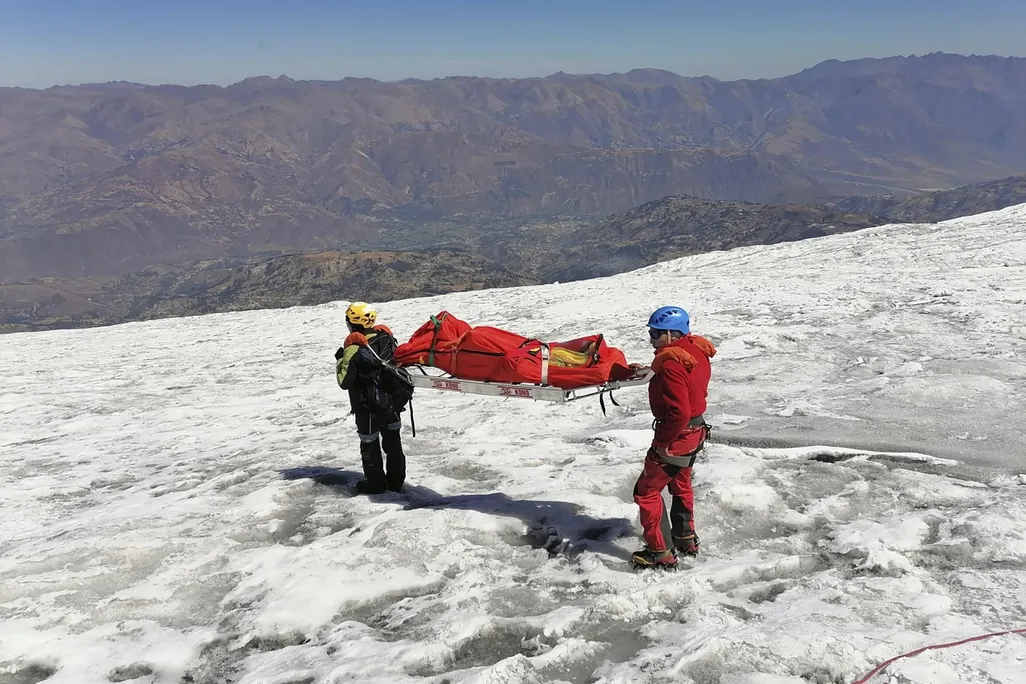 Two rescuers carrying a stretcher down a snowy mountain slope