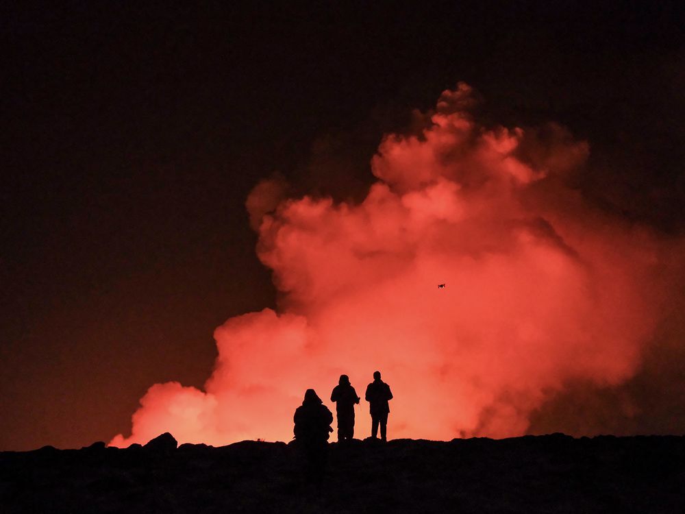 People in silhouette standing in front of a tall plume of smoke