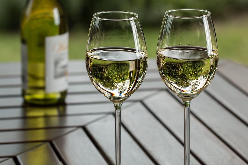 Pair of wine glasses full of white wine sitting on a table next to a bottle of white wine