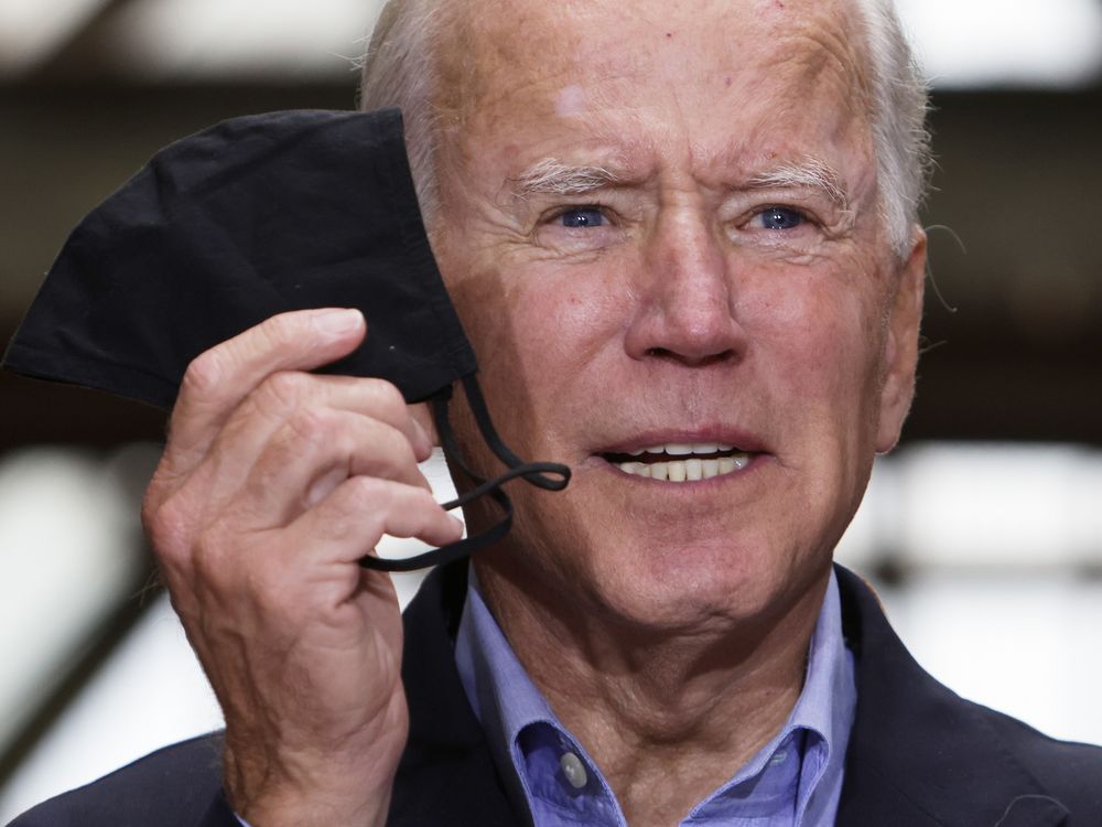 An image of President Joe Biden holding up a black mask as he speaks.