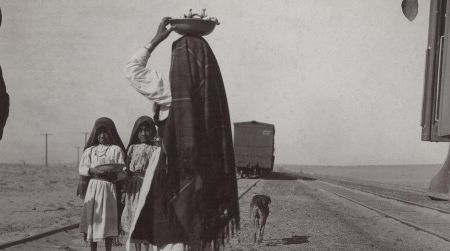 An Isleta woman and her children sell goods alongside a train track, circa late 1880s to early 1900s