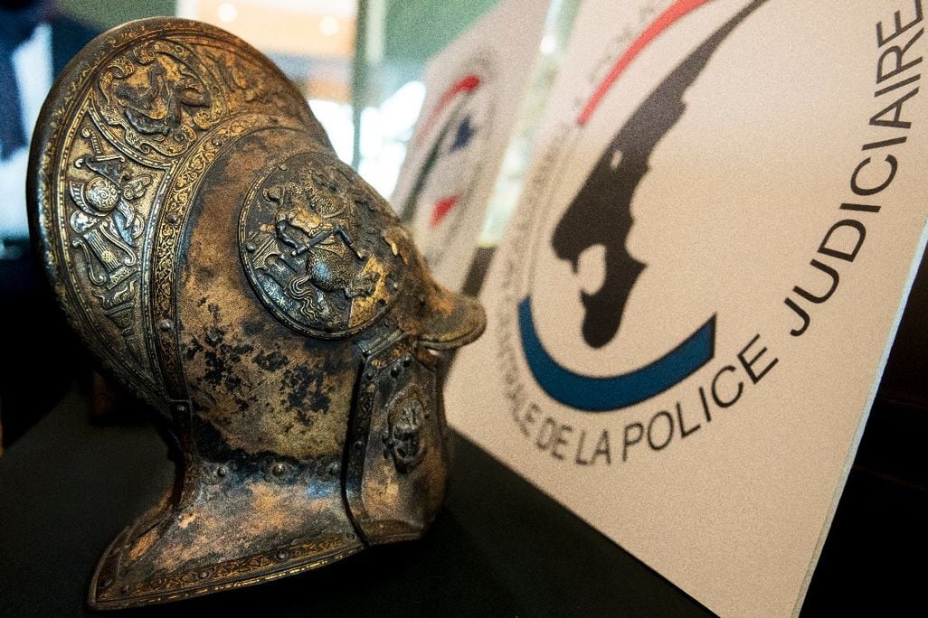 A close up look at an intricately carved helmet, with motifs of flowers, swords, torches and warriors on it