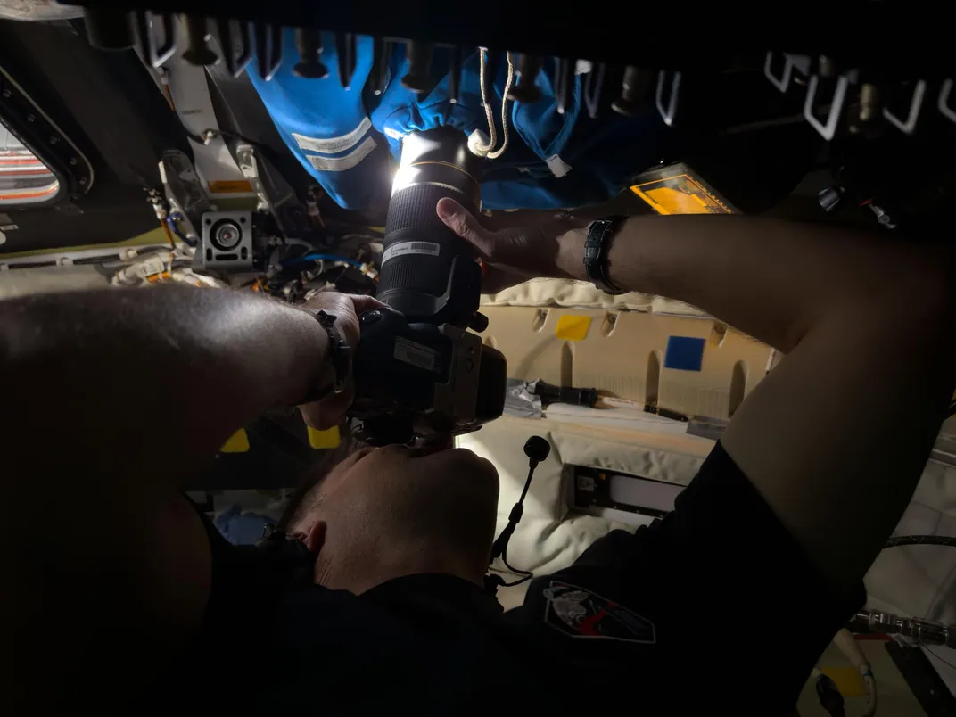 view from below as a man puts a camera through a hole in a blue curtain