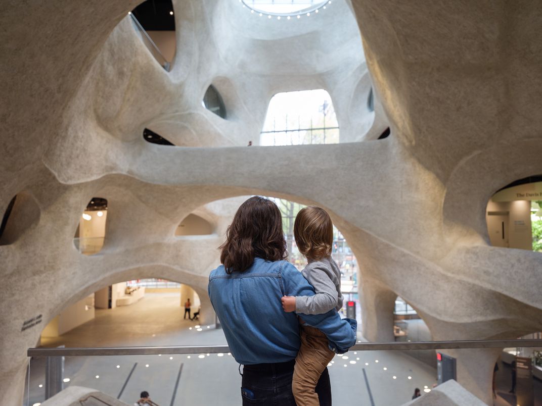 person holding child stand in front of the cavern-like atrium with a skylight