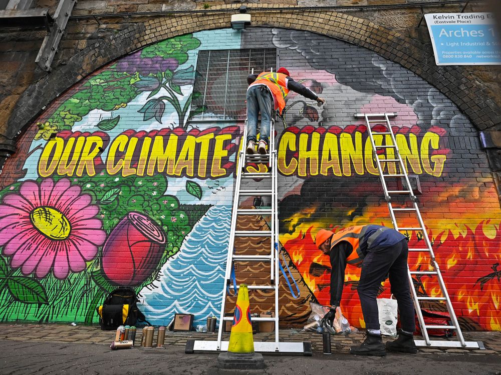 An colorful mural that reads "our climate in changing" with two people painting