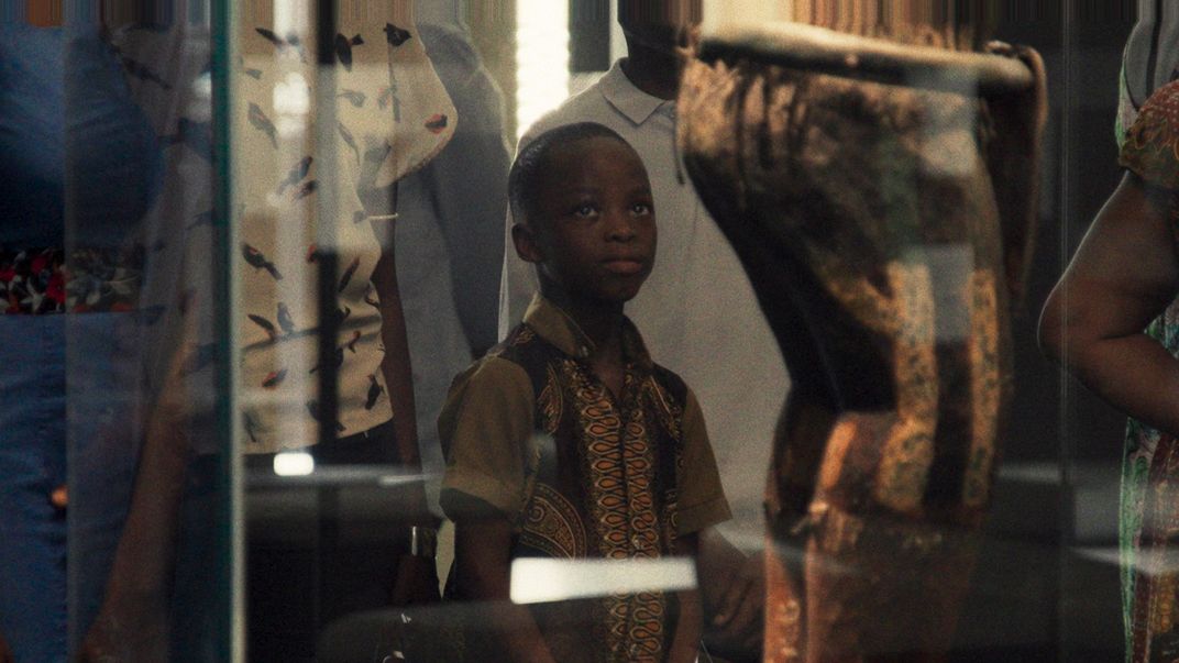 A boy looks up towards a wooden statue displayed behind glass.