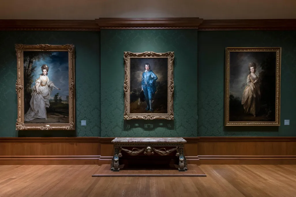 A dark green room with The Blue Boy hanging in the center of the frame and two other portraits on either side of him