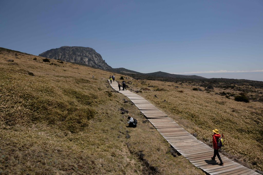 Hikers walking up wooden boardwalk toward a mountain