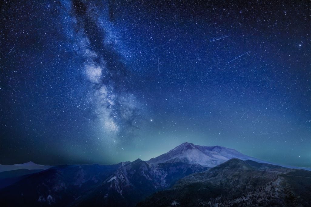 the milky way, several stars, and a few streaks of light left by burning meteors over a mountainous landscape