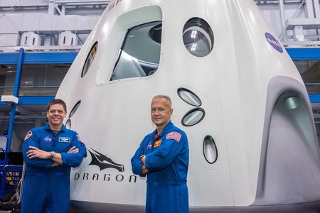 Commercial crew astronauts Bob Behnken (left) and Doug Hurley (right) stand in front of a SpaceX Dragon mock-up at the Johnson Space Center. 