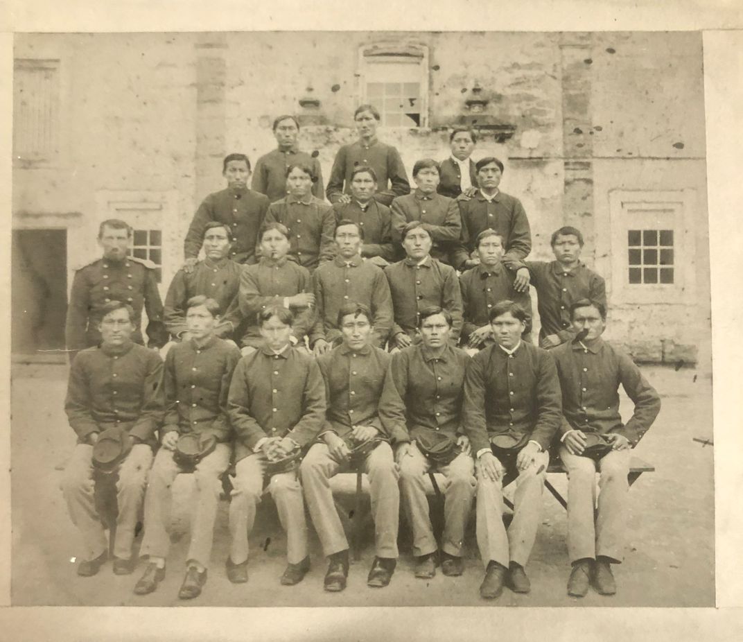 Group of Native American men in uniforms standing outside in front of building.